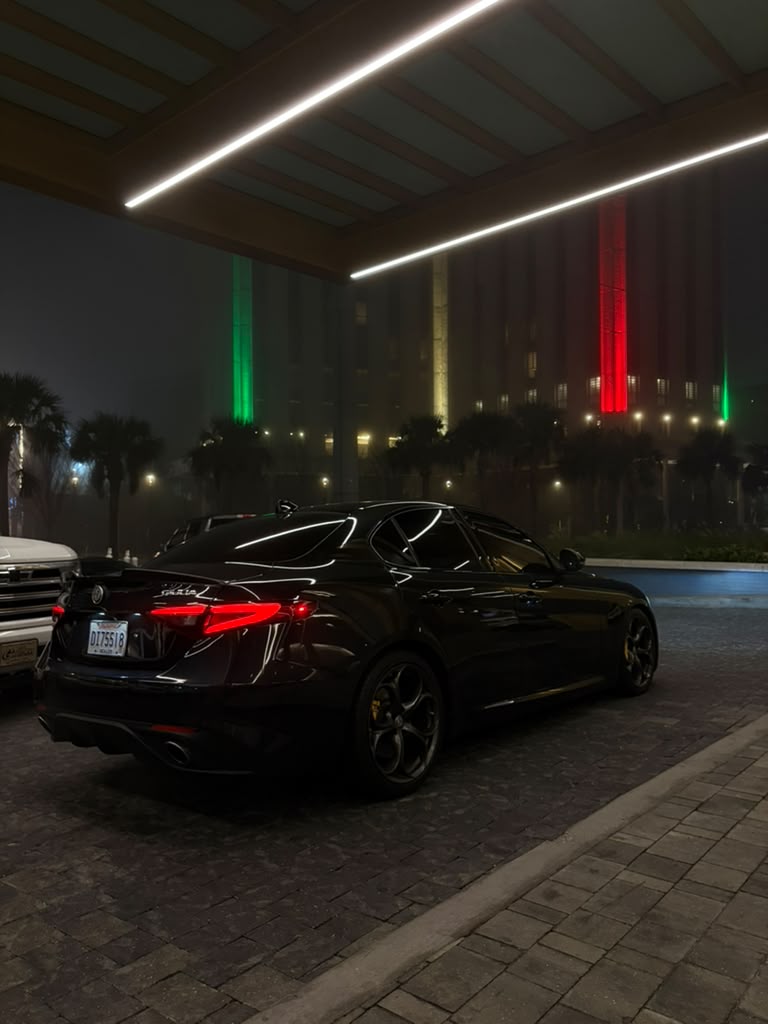 Black Alfa Romeo parked beneath illuminated roof beams at night